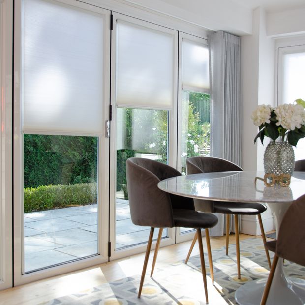 white honeycomb pleated blinds paired with silver voiles on bi-fold doors in dining room