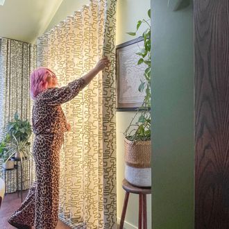 A-woman-in-leopard-print-pants-hangs-curtains-in-the-dining-room-of-Kiwi-Curtain