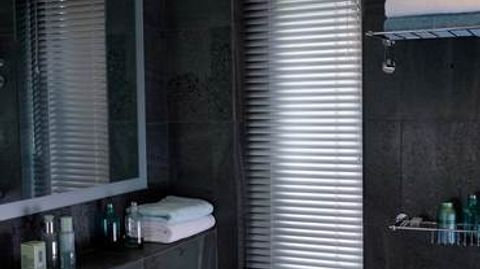 Silver venetian blind attached to a tall rectangular window in a bathroom decorated with dark slate tiles