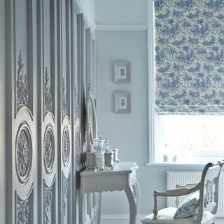 Large white room with ornate wooden panels on the walls and two Roman blinds fitted to the windows in Toile French Blue fabric