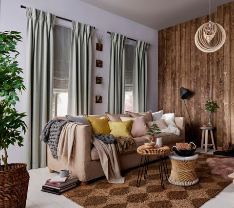 Rustic, cosy Living Room with two windows dressed with Lindora Silver Curtains and Howard Chartreuse Roman Blinds behind a sofa with cushions and blankets