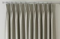 A cream coloured curtain on a curtain rail with a double pinch pleat header 