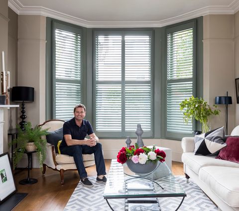 George Clarke sat in a Living Room with Full Height Shutters in a Bay Window