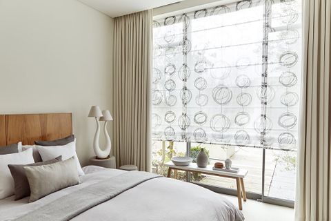 Bedroom with minimalist decor and curtains layered over Voile Roman blinds