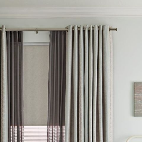 A cosy bedroom with Plain Curtains layered with voiles and blinds
