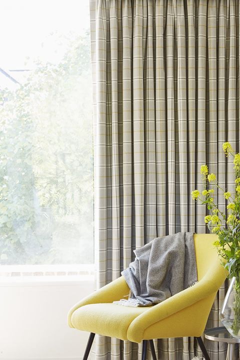 Bright yellow armchair in front of patterned cream curtains 