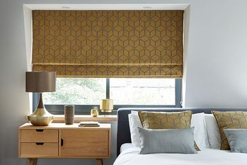 nexus brushed gold geometric pattern roman blinds in a bedroom window 