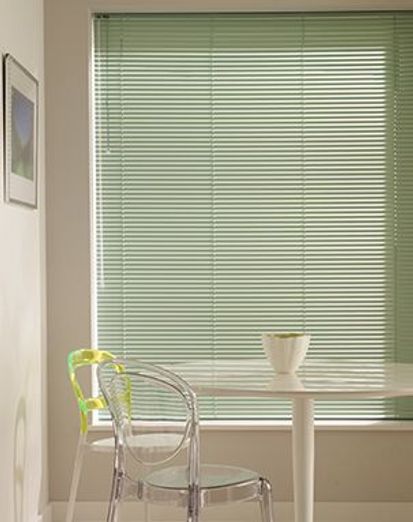 Green coloured venetian blind fitted to a large window in a cream decorated kitchen with transparent chairs and table