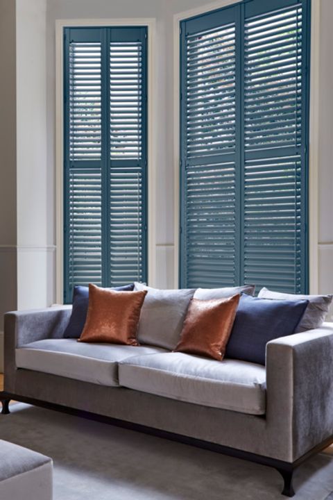 Blue tier on tier shutters fitted to a bay window in a living room with a grey sofa