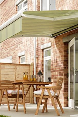 A green awning hanging over a patio with wooden garden furniture including chairs and a table