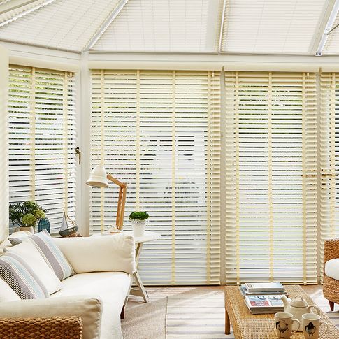 cream coloured faux wood wooden blinds fitted to door windows in a conservatory with a wicker sofa, chairs and white walls