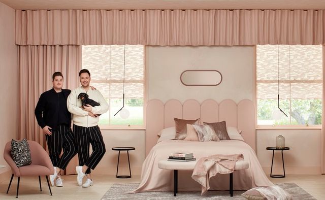 A bedroom decorated with blush and white colours has blush coloured curtains that span across two rectangular windows 