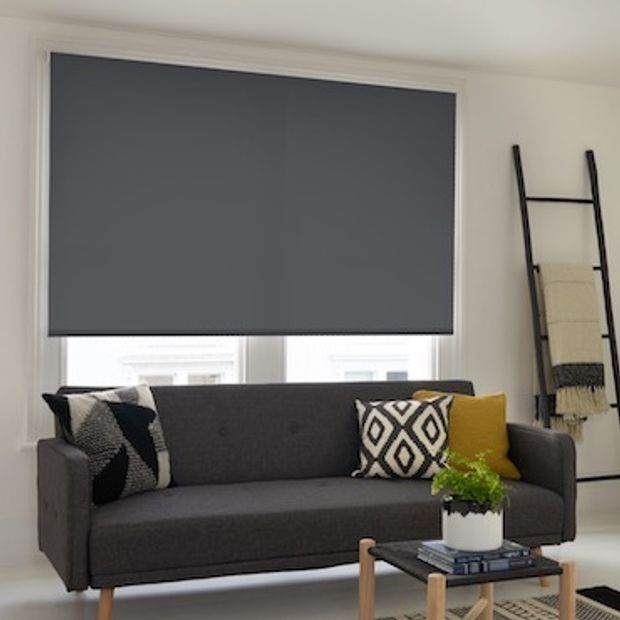 Acacia gunmetal roller blind fitted to a large window in a living room with a grey sofa