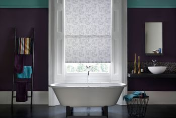 Modern bathroom with dark plum walls and sash windows dressed with grey pattern roller blind