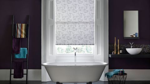 Modern bathroom with dark plum walls and sash windows dressed with grey pattern roller blind