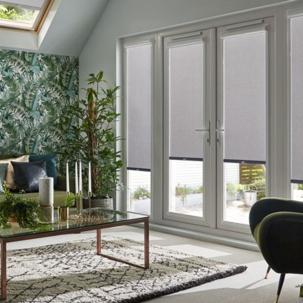 four light grey perfect fit blinds partially open on door length windows in a grey room with green furnishings and plants including a feature wall of plant themed wallpaper
