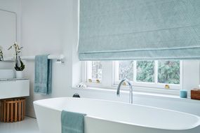 Bathroom with large ceramic white tub and sash windows dressed with pastel blue roman blinds