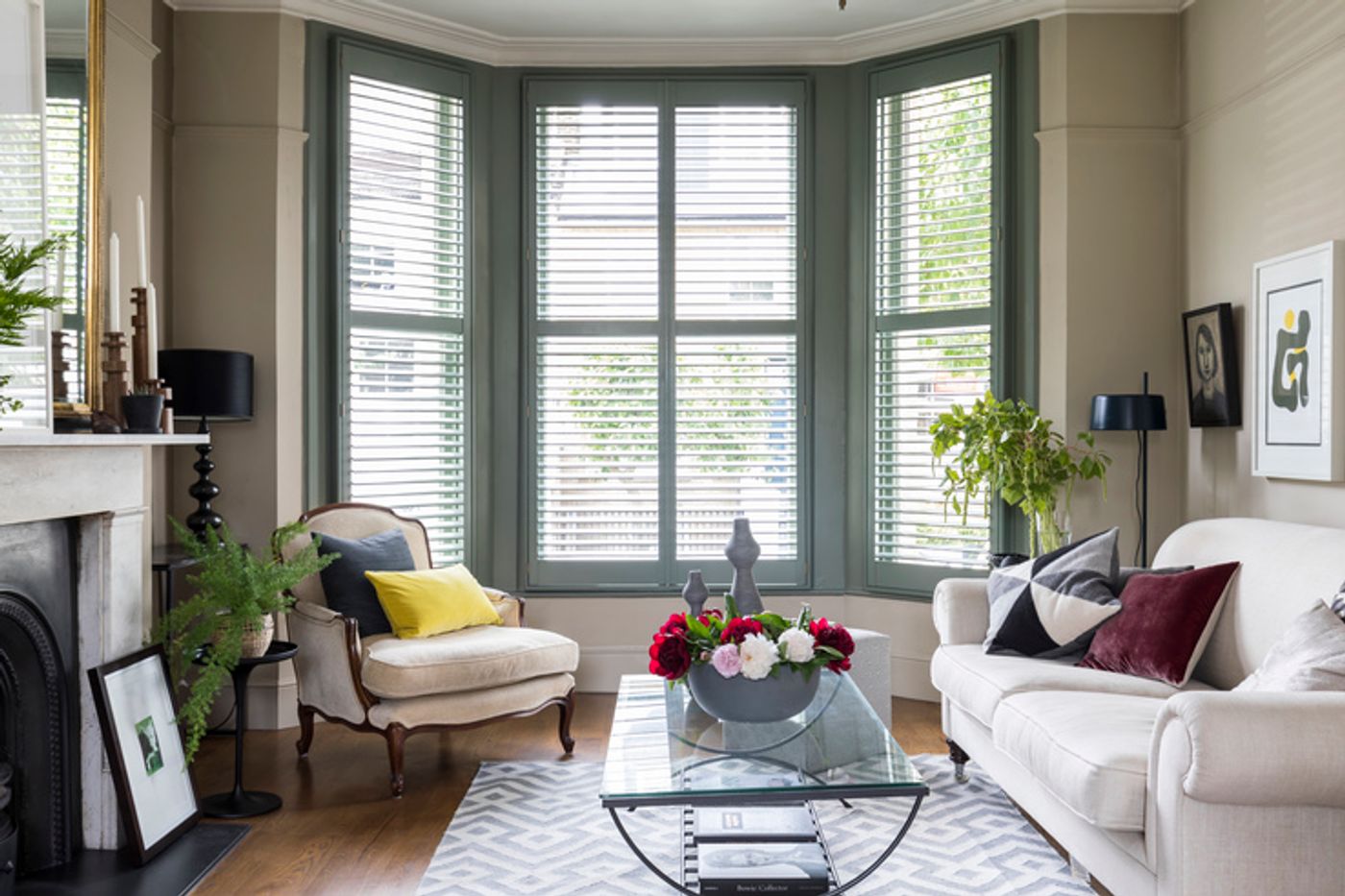 Green full height shutters fitted to bay windows in a living room decorated in cream colours