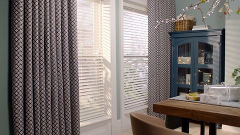 Festive dining area with a window dressed with white venetian blinds and luxurious print curtains