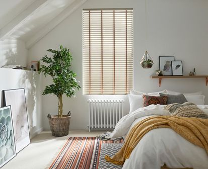 Cosy, natural bedroom with house plants and scandi design features and a window dressed with faux wood venetian blinds
