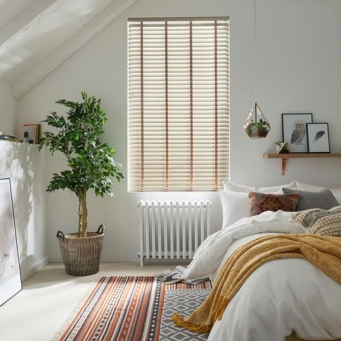Cosy, natural bedroom with house plants and scandi design features and a window dressed with faux wood venetian blinds