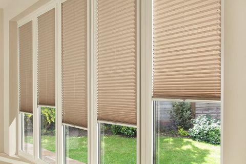 A series of window panels covered by roller blinds in a light tan shade