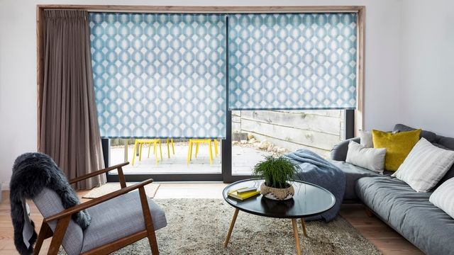 A brown coloured curtain matched with blue and white geometrically patterned roller blinds in a living room