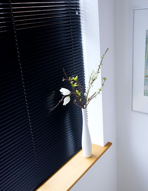 A close up of a black blind in a white room with a white vase