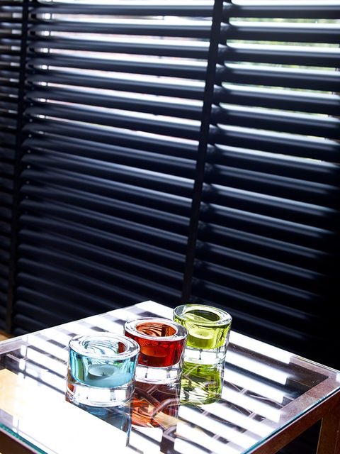 Close up of jet black Venetian blinds with three brightly coloured candles in front 