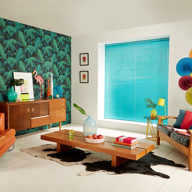 A bright blue Venetian blind in a neutral room featuring orange furniture and a blue and green feature wall.