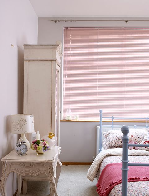 A pink Venetian blind hangs in a child's room behind a bed