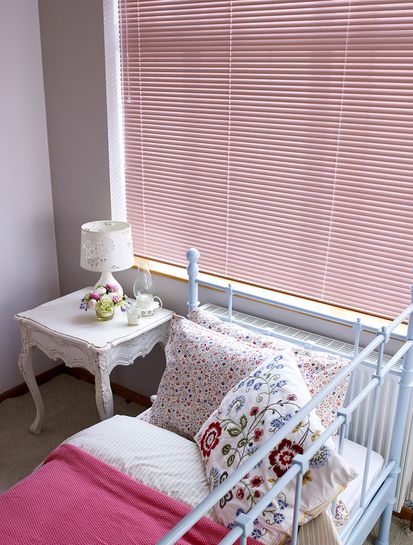 Close up of a child's bed and window covered in a pink Venetian blind