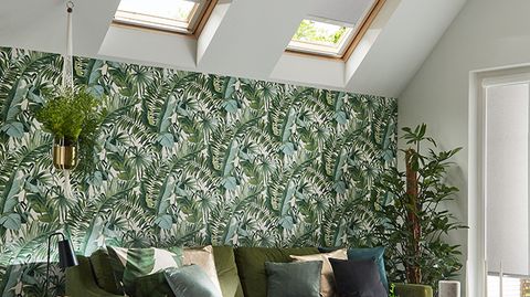 Skylight blinds in Acacia Silver are fitted to two skylight windows in a living room decorated in floral colours including the wallpaper, sofa and various plants