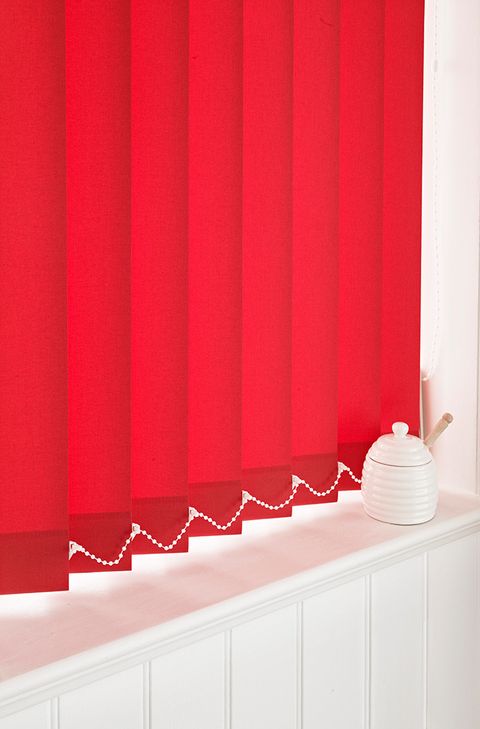 Red vertical blinds which are opened slightly and fitted to a window in a room decorated in white