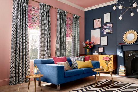 Grey curtains fitted with pink and blue florally patterned roman blinds in a living room decorated with pink and navy blue walls