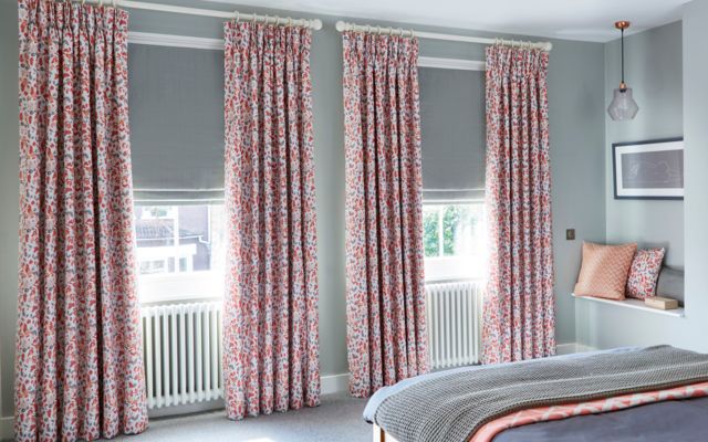 Curtains decorated with red coloured blossom are matched with grey roman blinds in a grey decorated bedroom
