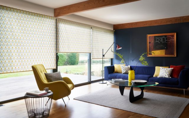 Yellow roller blinds fitted with wide windows in a living room decorated in white, yellow armchair and a blue sofa