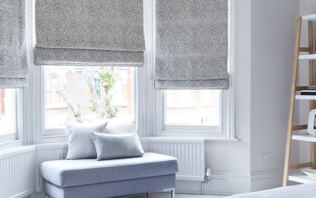 Grey roman blinds fitted to bay shaped windows in a living room decorated in white 