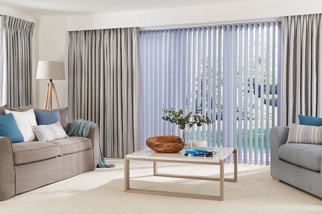 Blue vertical blinds fitted to a door window and matched with grey curtains in a living room decorated in white and grey sofas