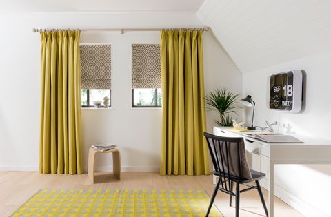 Grey roman blinds on small windows with yellow curtains in a study decorated in white