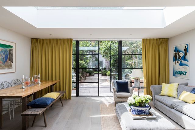 Yellow curtains fitted to a wide door windows that open onto a patio in a kitchen featuring a dining table and sofa