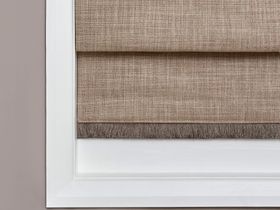 Sand coloured roman blind with brown fringing fitted to a window in a room with beige coloured walls