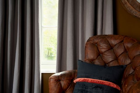 Close up detail of leather armchair in front of single window dressed with curtains