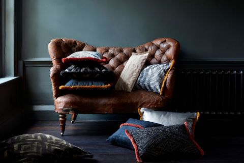 Cushions part of the Abigail Ahern collection of fabrics surround a brown leather chair in a rustic home