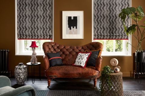 Edgy living room with brown leather sofa and two windows dressed with grey pattern roman blinds