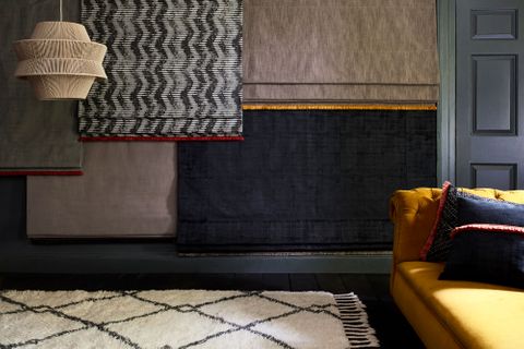 A collection of different roman blinds hanging from a wall in a living room including cley donkey, cadillac noir, garratt bullrush, amis buff, and cley mole