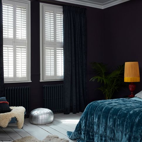 Black coloured cley mole curtains matched with white tier on tier shutters in a bedroom decorated with navy blue walls.