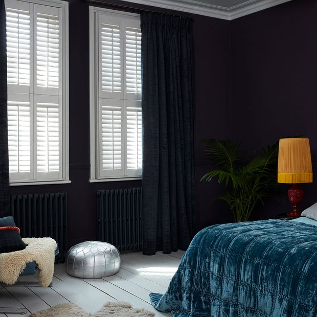 Black coloured cley mole curtains matched with white tier on tier shutters in a bedroom decorated with navy blue walls.