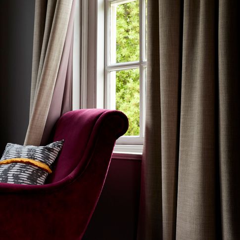 Beige coloured curtains fitted to a tall window in a room with a purple velvet armchair