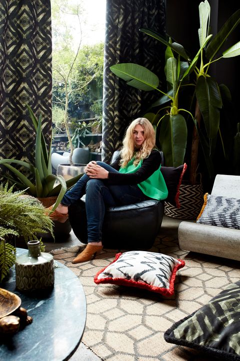 Abigail Ahern sat in a living room decorated with a range of plants and geometrically styled cushions, rug and curtains in black and white
